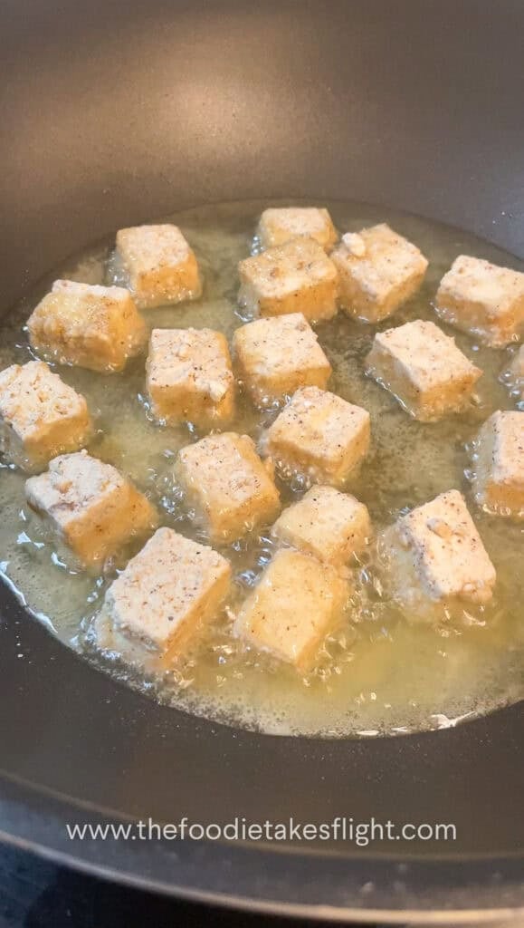 Tofu cubes sizzling in a pan as they shallow fry to a crisp golden brown.