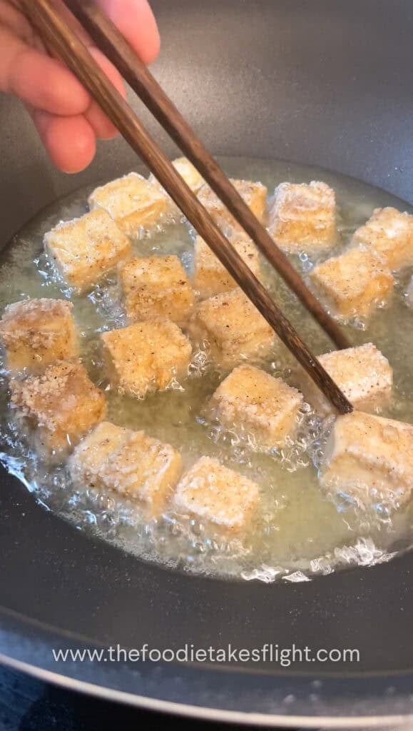 Tofu cubes sizzling in a pan as they shallow fry to a crisp golden brown.