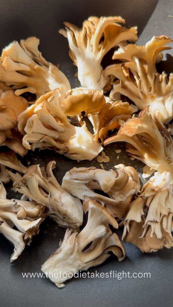 Maitake mushroom clusters dry-searing in a wok to develop golden charred edges