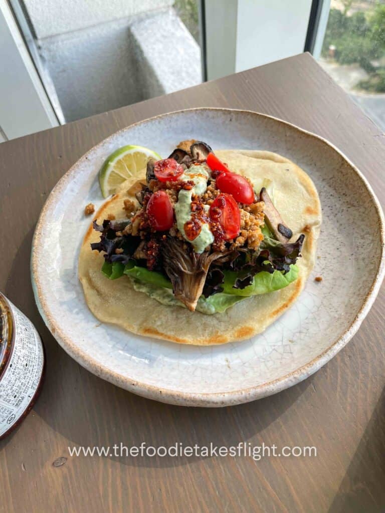 Pita bread topped with lettuce, tomato, crispy tofu, mushrooms, and a spoonful of pesto mayo