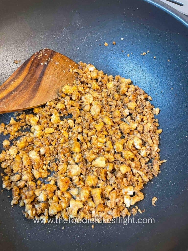 Crispy golden tofu pieces being sautéed in a pan with garlic and soy glaze