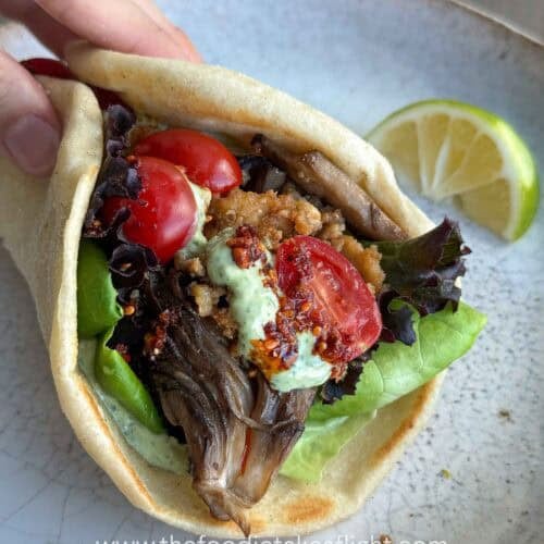 Pita bread topped with lettuce, tomato, crispy tofu, mushrooms, and a spoonful of pesto mayo