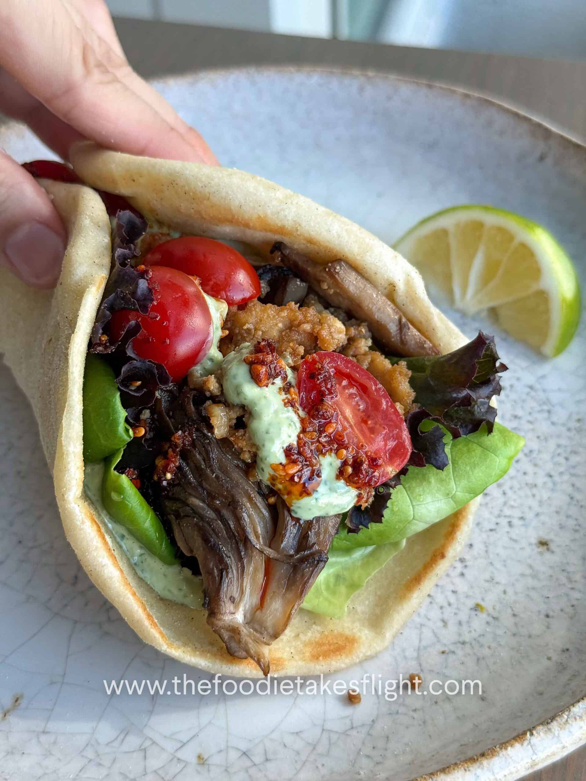 Pita bread topped with lettuce, tomato, crispy tofu, mushrooms, and a spoonful of pesto mayo