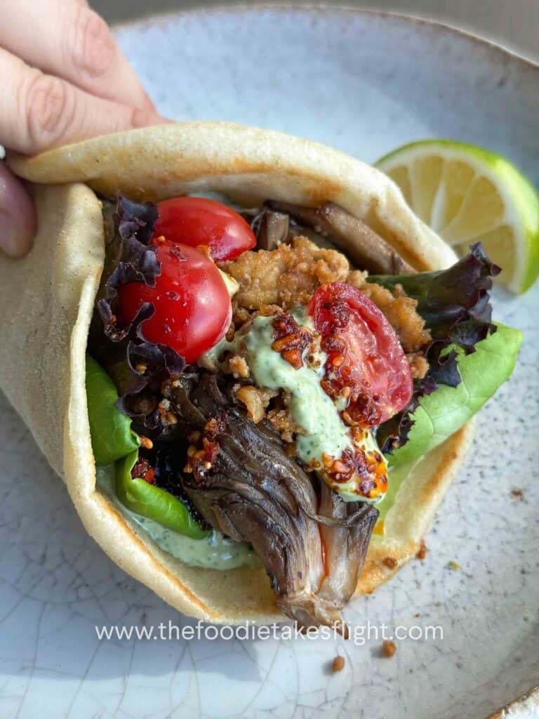 Pita bread topped with lettuce, tomato, crispy tofu, mushrooms, and a spoonful of pesto mayo