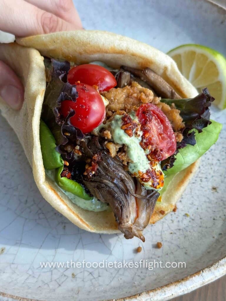 Pita bread topped with lettuce, tomato, crispy tofu, mushrooms, and a spoonful of pesto mayo