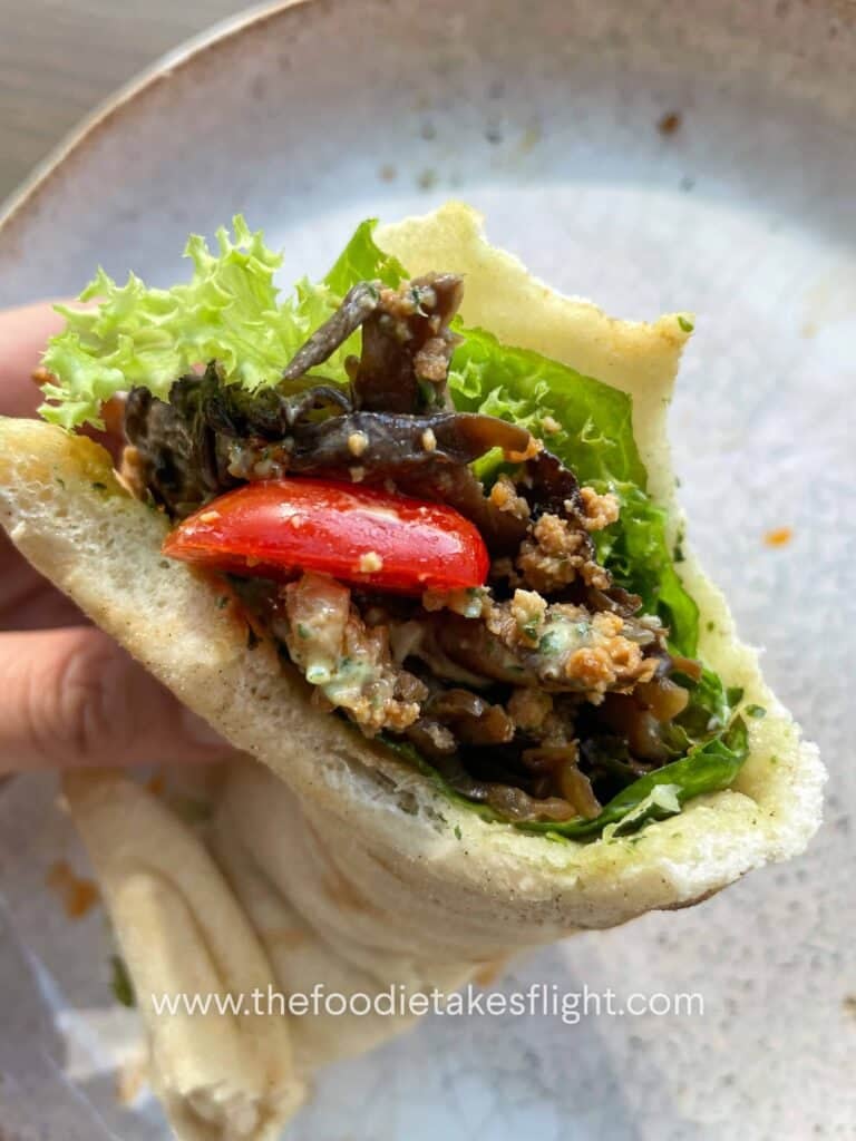Pita bread topped with lettuce, tomato, crispy tofu, mushrooms, and a spoonful of pesto mayo