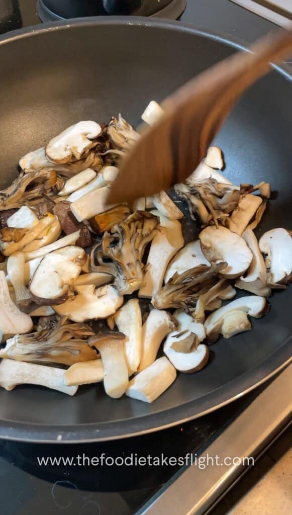 Sliced mushrooms and onions sautéing in vegan butter with steam rising from the skillet