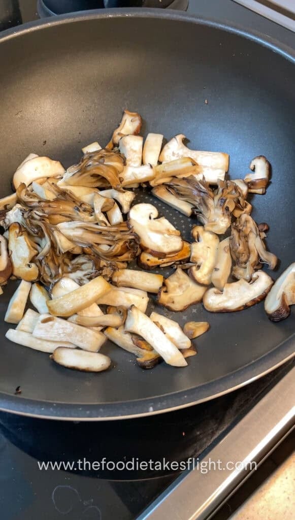 Sliced mushrooms and onions sautéing in vegan butter with steam rising from the skillet