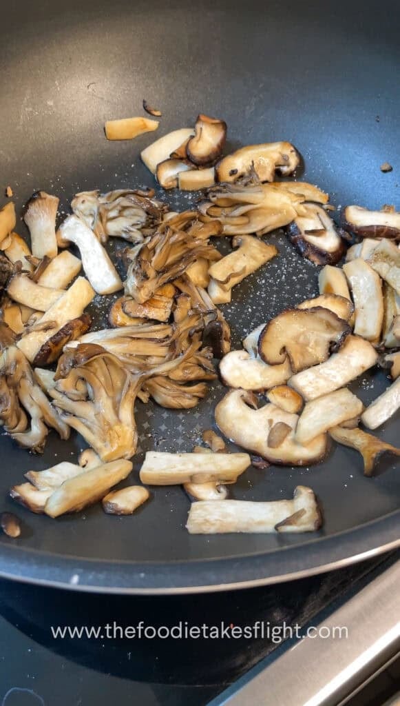 Sliced mushrooms and onions sautéing in vegan butter with steam rising from the skillet