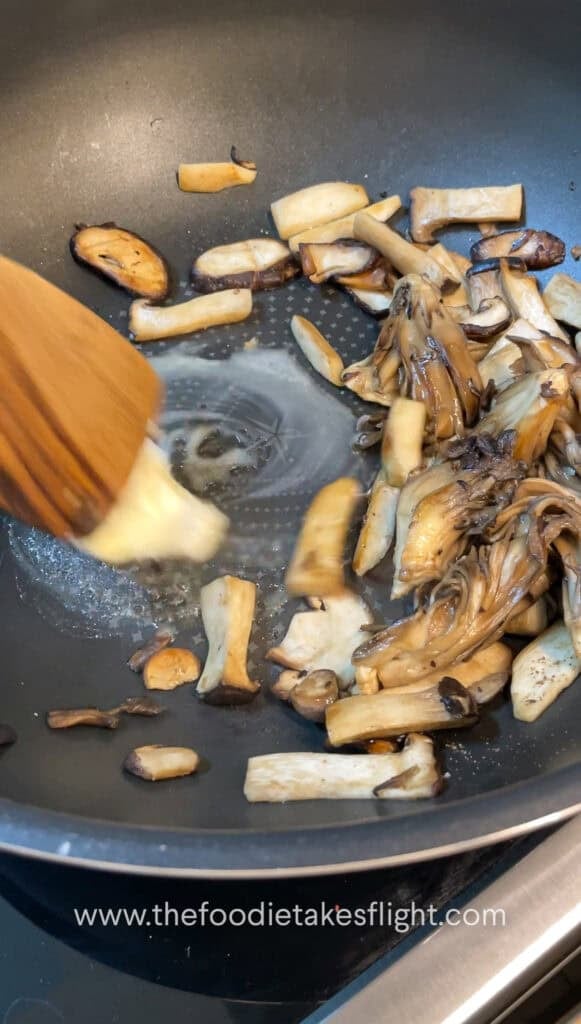 Sliced mushrooms and onions sautéing in vegan butter with steam rising from the skillet