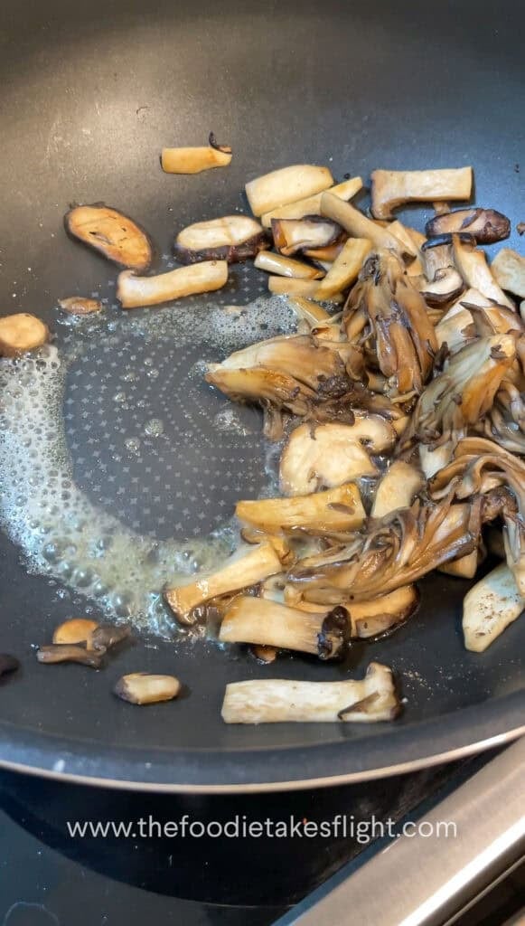 Sliced mushrooms and onions sautéing in vegan butter with steam rising from the skillet
