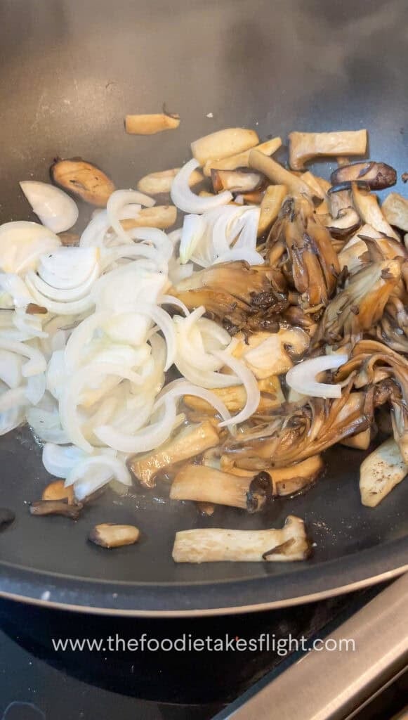 Sliced mushrooms and onions sautéing in vegan butter with steam rising from the skillet