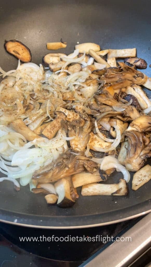 Sliced mushrooms and onions sautéing in vegan butter with steam rising from the skillet