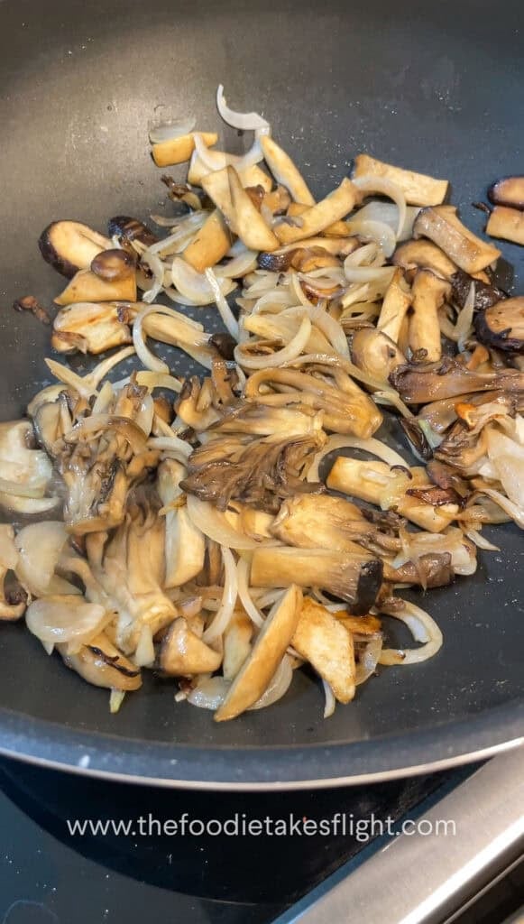 Sliced mushrooms and onions sautéing in vegan butter with steam rising from the skillet