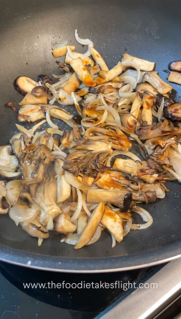 Sliced mushrooms and onions sautéing in vegan butter with steam rising from the skillet