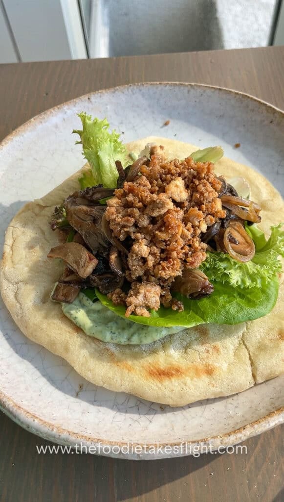 Pita bread topped with lettuce, crumbled tofu, mushrooms