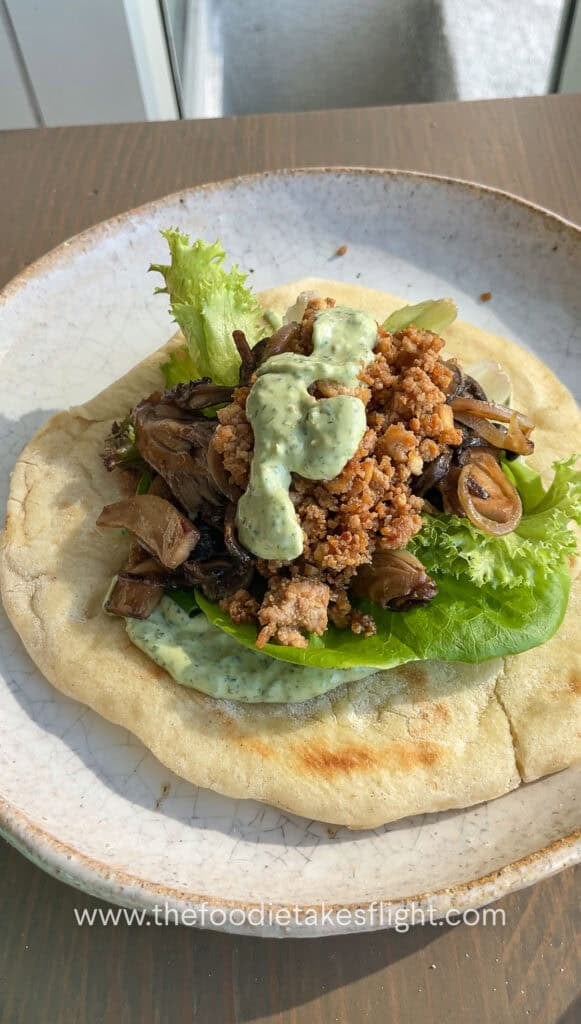 Pita bread topped with lettuce, tomato, crispy tofu, mushrooms, and a spoonful of pesto mayo