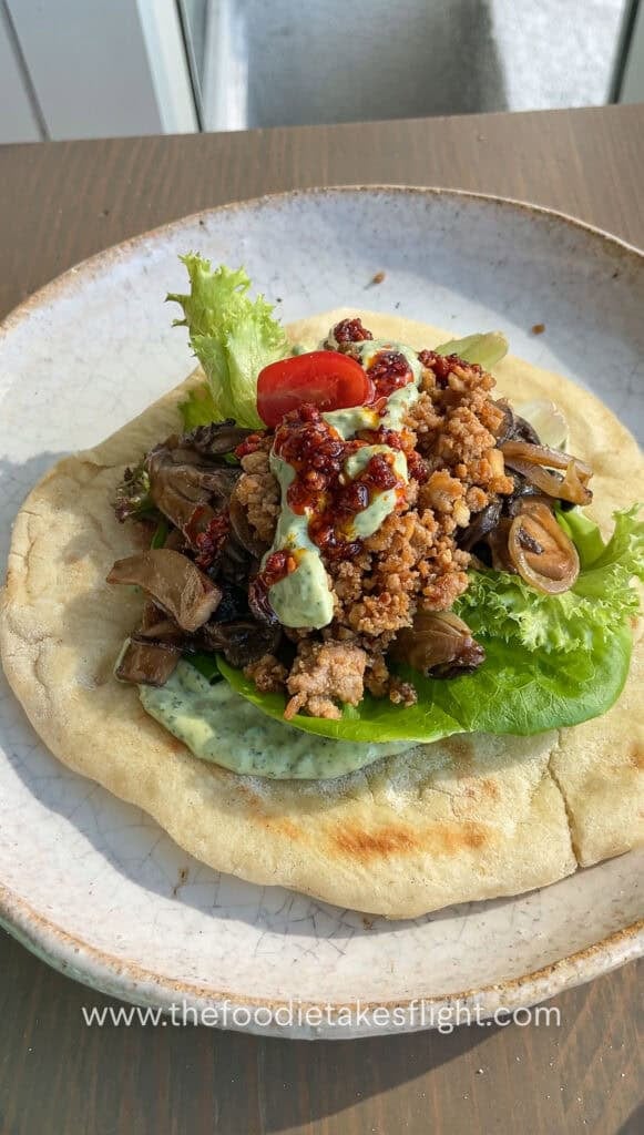Pita bread topped with lettuce, tomato, crispy tofu, mushrooms, and a spoonful of pesto mayo