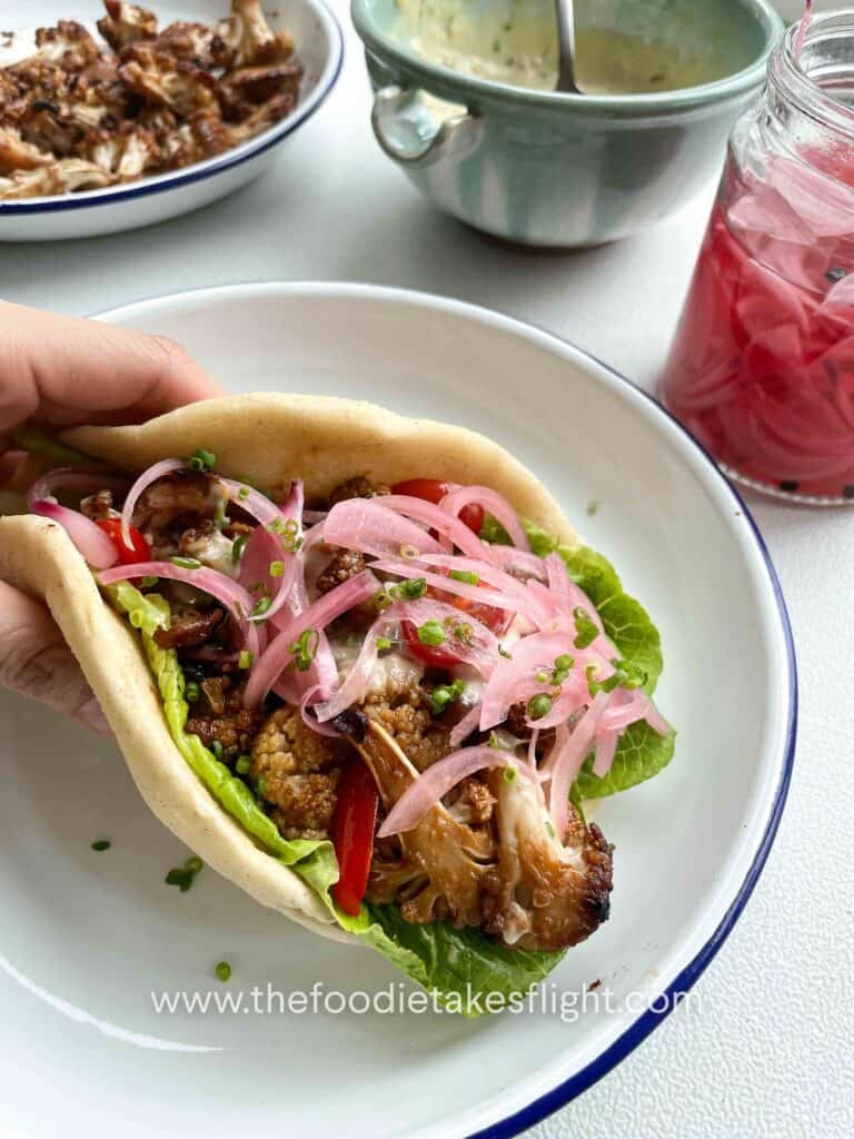 Pita wraps filled with roasted miso cauliflower, lettuce, tomatoes, pickled onions, and a drizzle of roasted garlic mayo