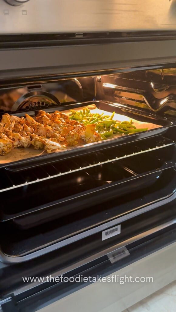 cauliflower and peppers on a parchment paper lined baking tray in the oven