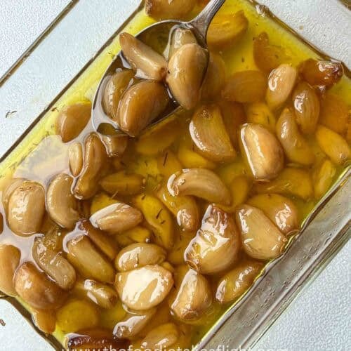 Soft, golden garlic cloves glistening in infused oil after roasting