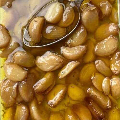 Soft, golden garlic cloves glistening in infused oil after roasting