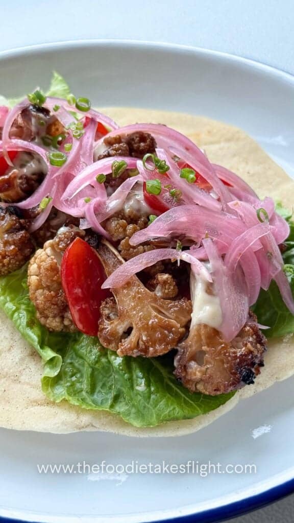 Pita wraps filled with roasted miso cauliflower, lettuce, tomatoes, pickled onions, and a drizzle of roasted garlic mayo