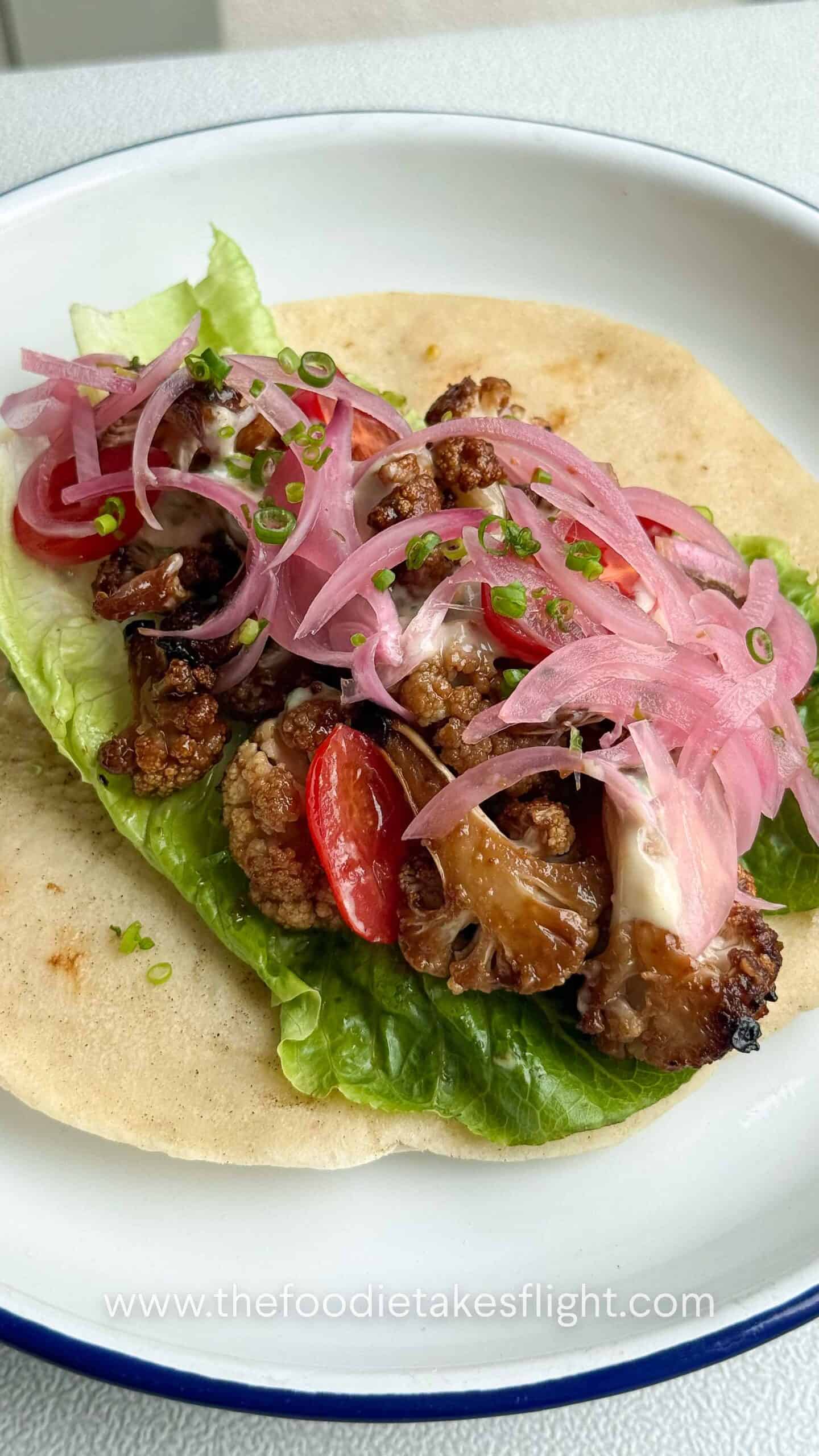 Pita wraps filled with roasted miso cauliflower, lettuce, tomatoes, pickled onions, and a drizzle of roasted garlic mayo