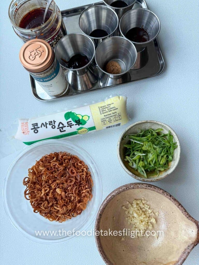 Raw silken tofu, garlic, shallot oil, soy sauces, vinegar, and chili crisp arranged on a prep surface