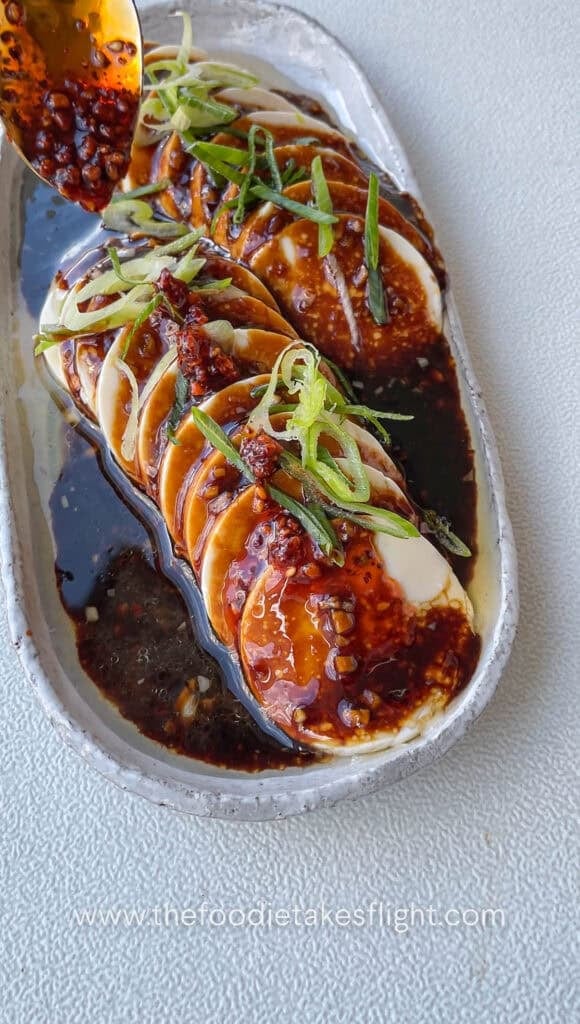 pouring the tasty shallot garlic oil sauce onto the cold silken tofu