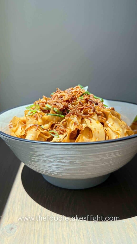 A bowl of shallot oil noodles topped with crispy fried shallots, scallions, and sesame seeds