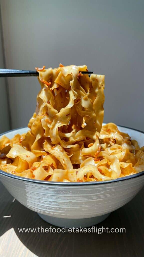Chopsticks lifting glossy noodles coated in shallot oil and soy sauce from a serving bowl