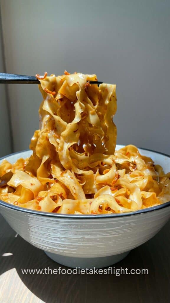 Chopsticks lifting glossy noodles coated in shallot oil and soy sauce from a serving bowl