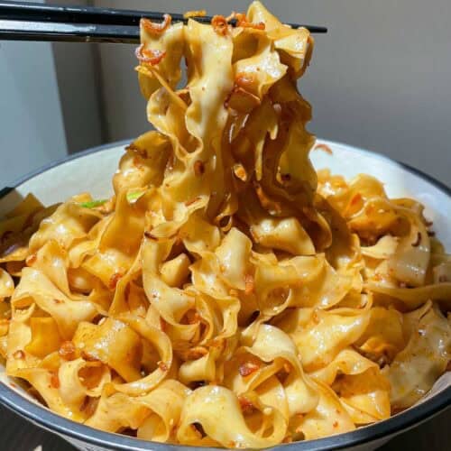 Chopsticks lifting glossy noodles coated in shallot oil and soy sauce from a serving bowl