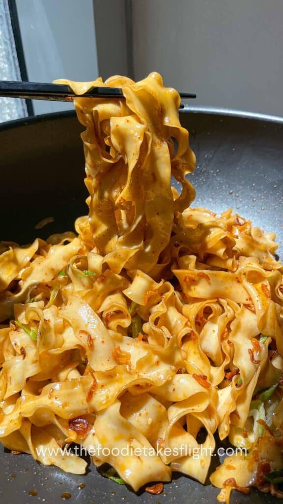 Chopsticks lifting glossy noodles coated in shallot oil and soy sauce