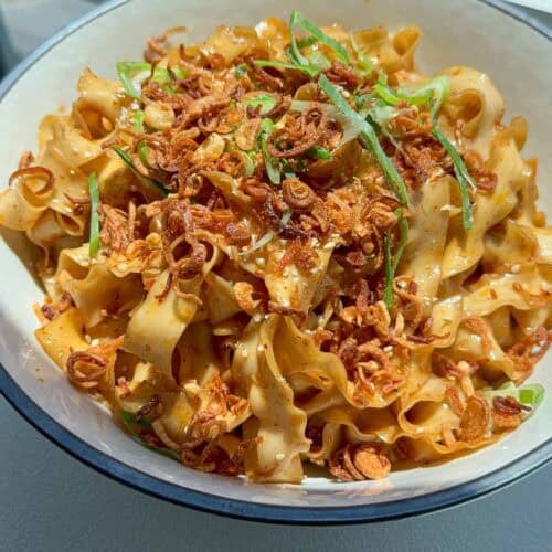 A bowl of shallot oil noodles topped with crispy fried shallots, scallions, and sesame seeds