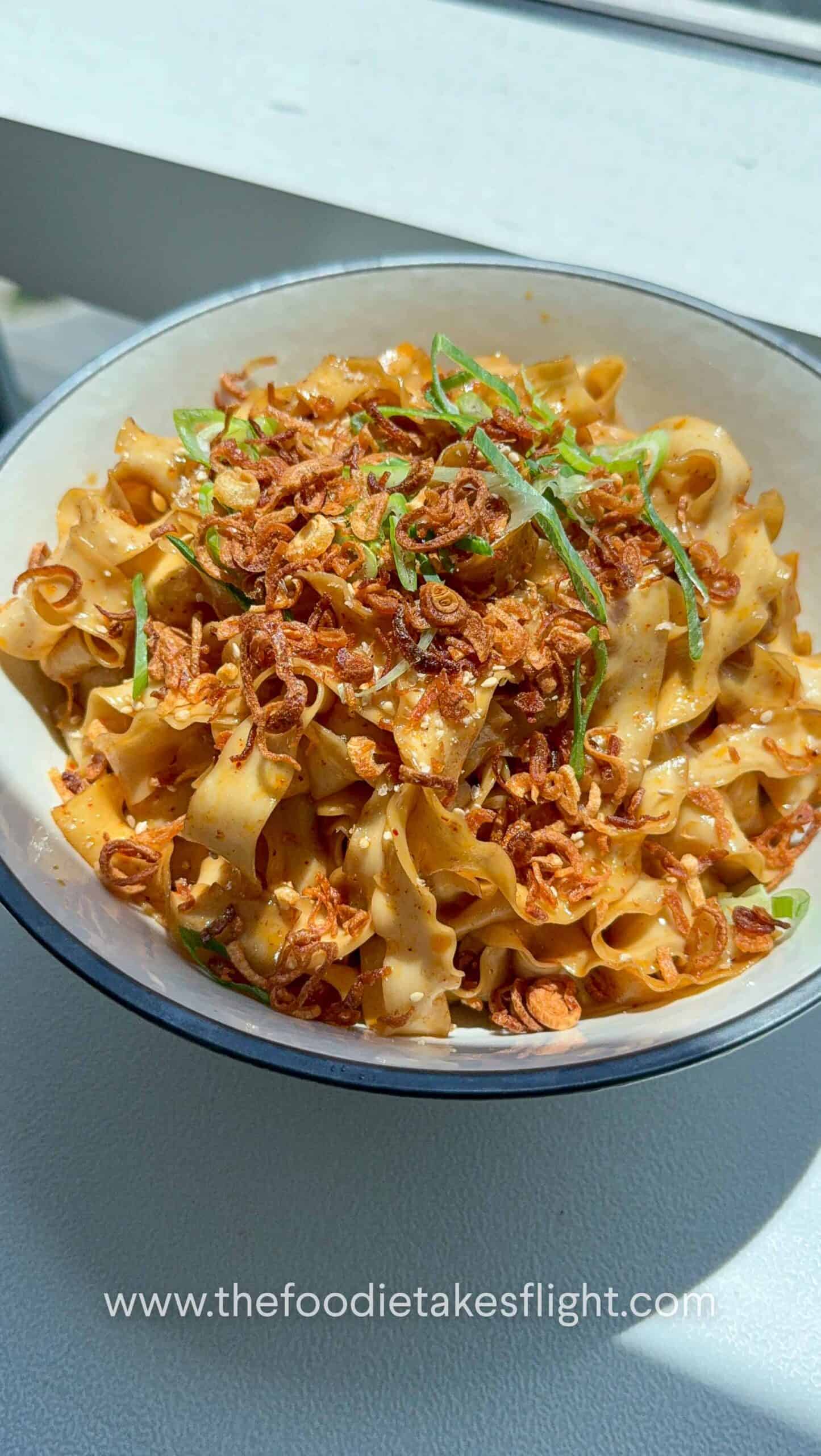 A bowl of shallot oil noodles topped with crispy fried shallots, scallions, and sesame seeds