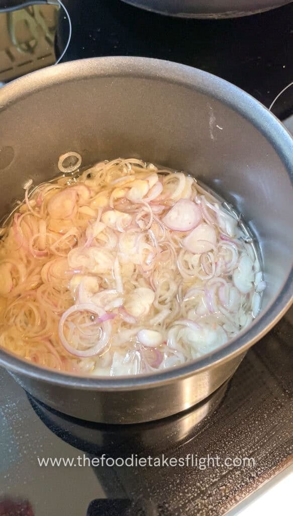 Thinly sliced shallots gently frying in neutral oil in a pot, bubbling as they crisp