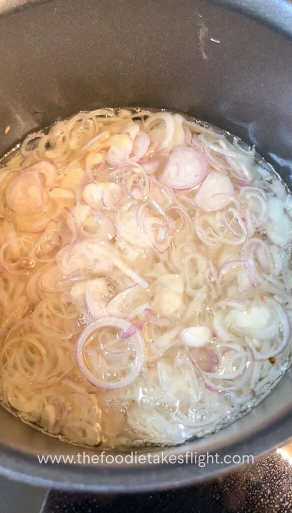 Thinly sliced shallots gently frying in neutral oil in a pot, bubbling as they crisp
