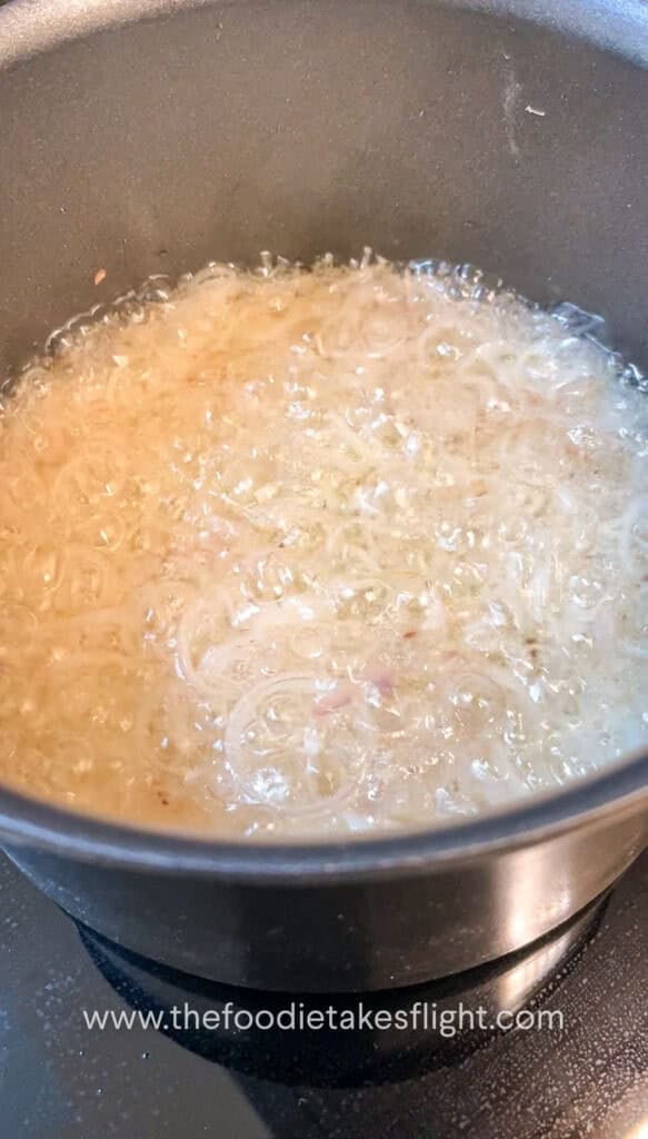 Thinly sliced shallots gently frying in neutral oil in a pot, bubbling as they crisp
