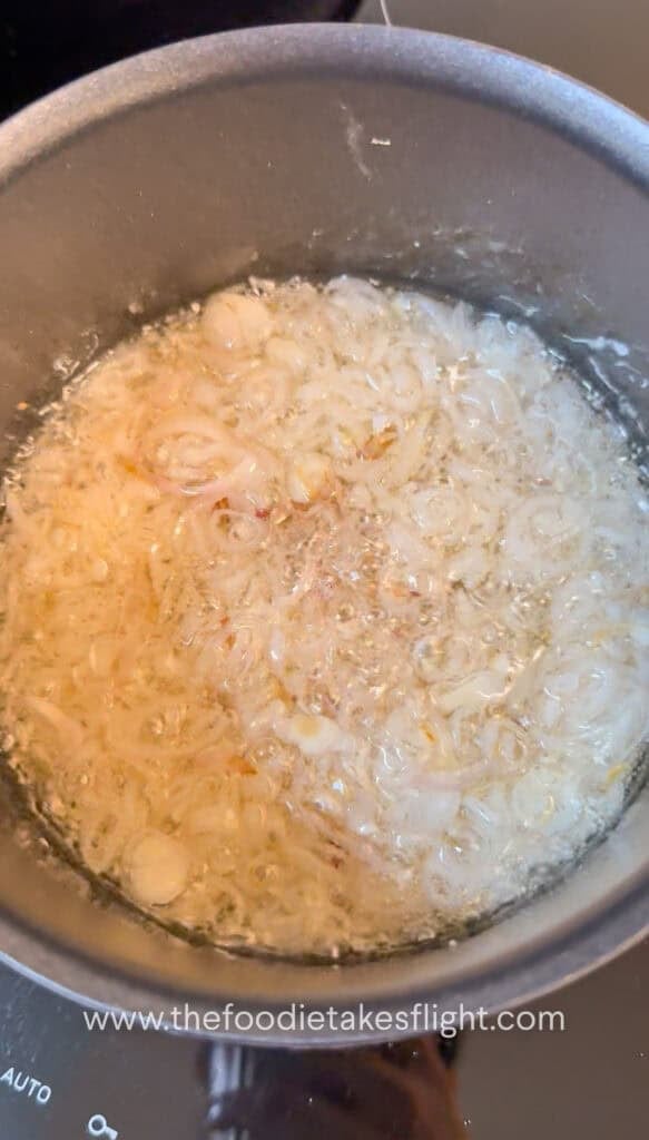 Thinly sliced shallots gently frying in neutral oil in a pot, bubbling as they crisp