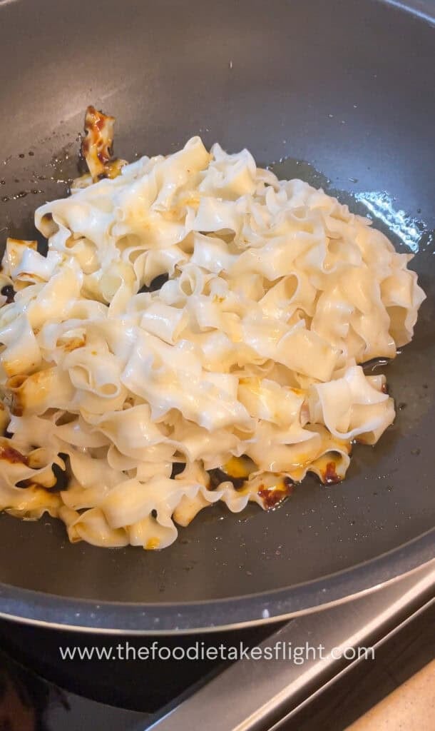 Wok of noodles being tossed in hot shallot oil with soy sauce and chili flakes