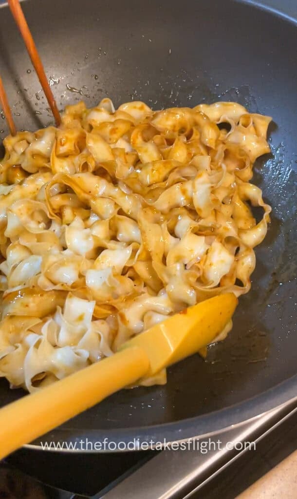 Wok of noodles being tossed in hot shallot oil with soy sauce and chili flakes