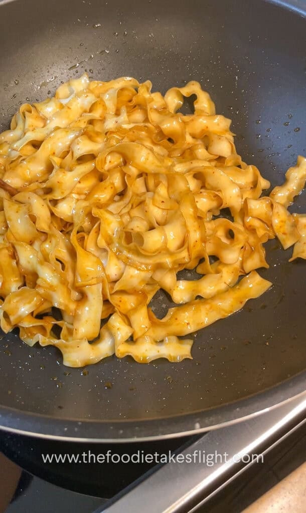 Wok of noodles being tossed in hot shallot oil with soy sauce and chili flakes