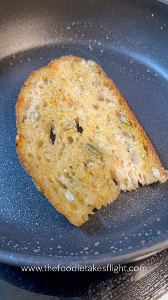 Slice of bread being toasted in a skillet with garlic oil until crisp and golden