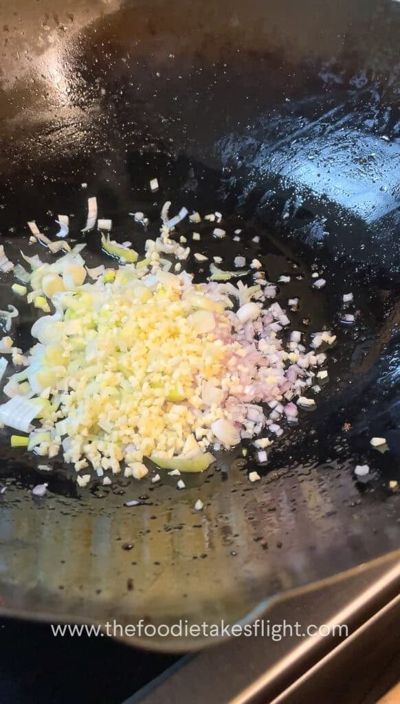 stir frying shallots, garlic, and onion in oil in a wok