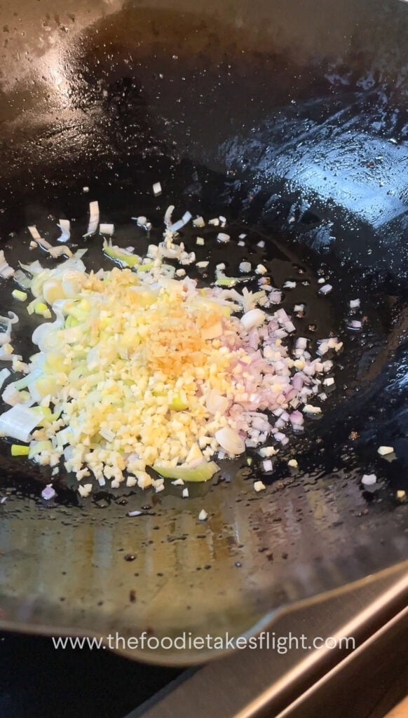 stir frying shallots, garlic, and onion in oil in a wok