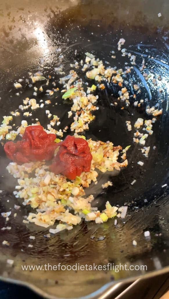 cooking down the tomato paste with aromatics in a wok