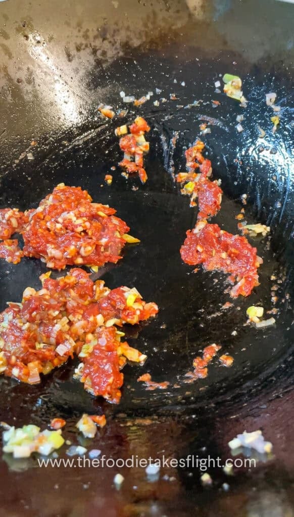 cooking down the tomato paste with aromatics in a wok