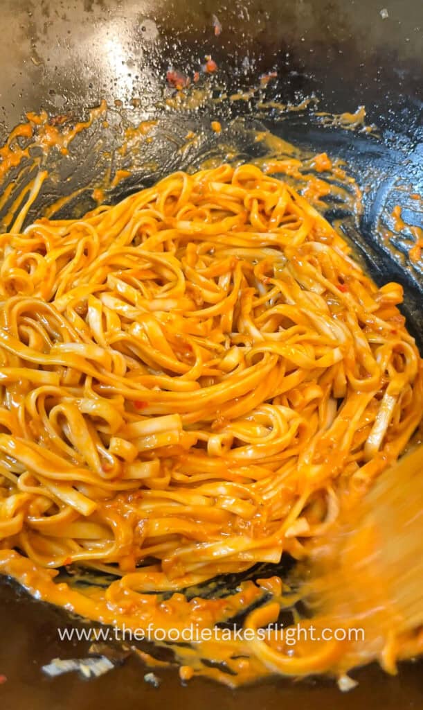 tossing cooked wheat noodles in creamy tomato coconut sauce